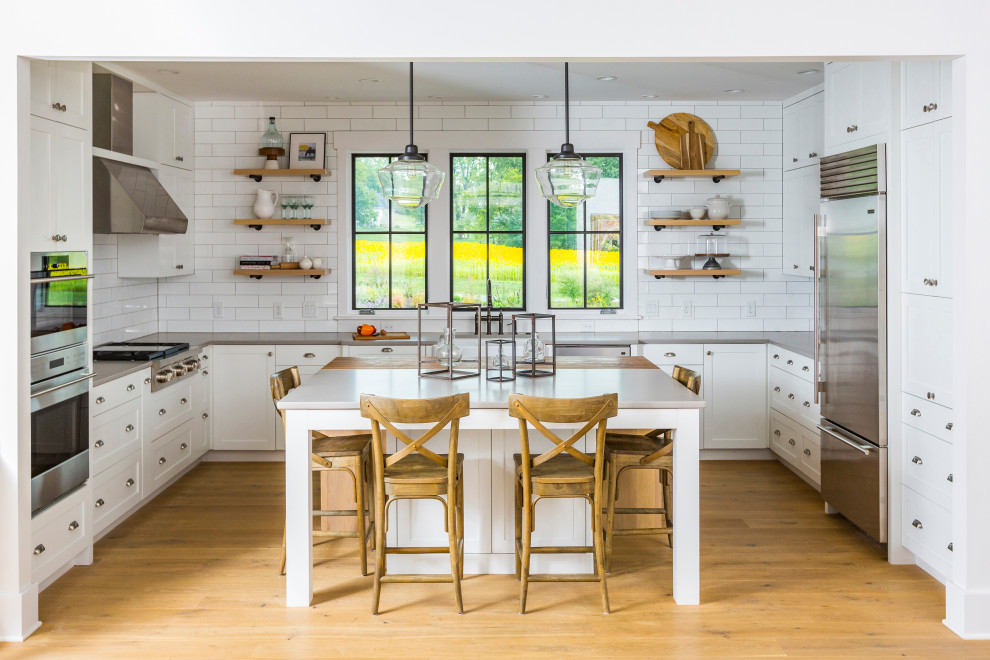 Lantlig inredning av ett grå grått kök, med en rustik diskho, luckor med infälld panel, vita skåp, bänkskiva i kvarts, vitt stänkskydd, stänkskydd i cementkakel, rostfria vitvaror, ljust trägolv, en köksö och gult golv