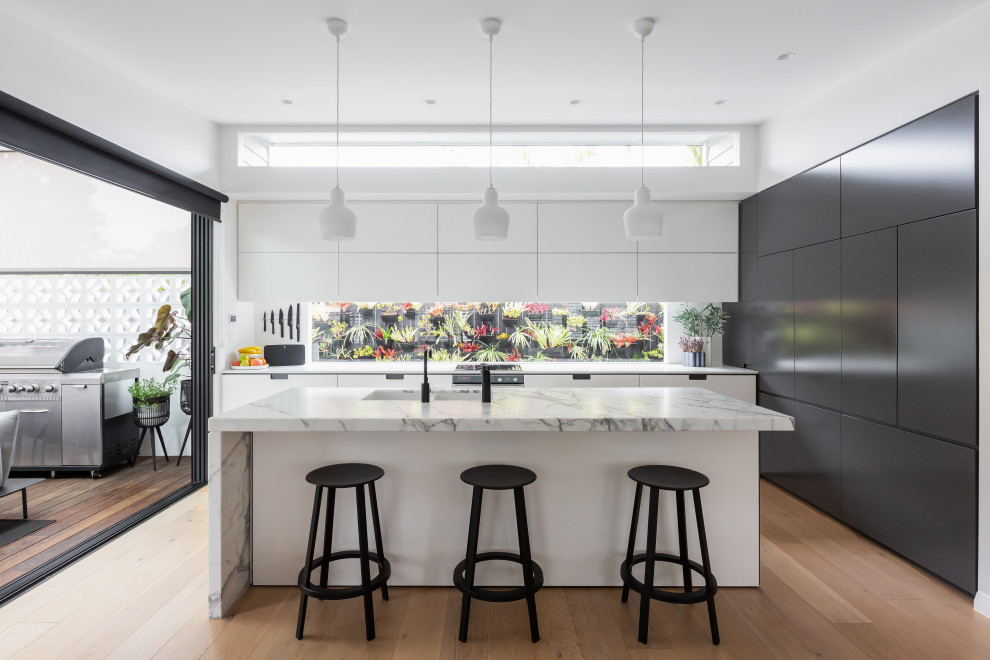 Design ideas for a large midcentury l-shaped eat-in kitchen in Sydney with a double-bowl sink, flat-panel cabinets, white cabinets, marble benchtops, window splashback, light hardwood floors, with island, brown floor and white benchtop.
