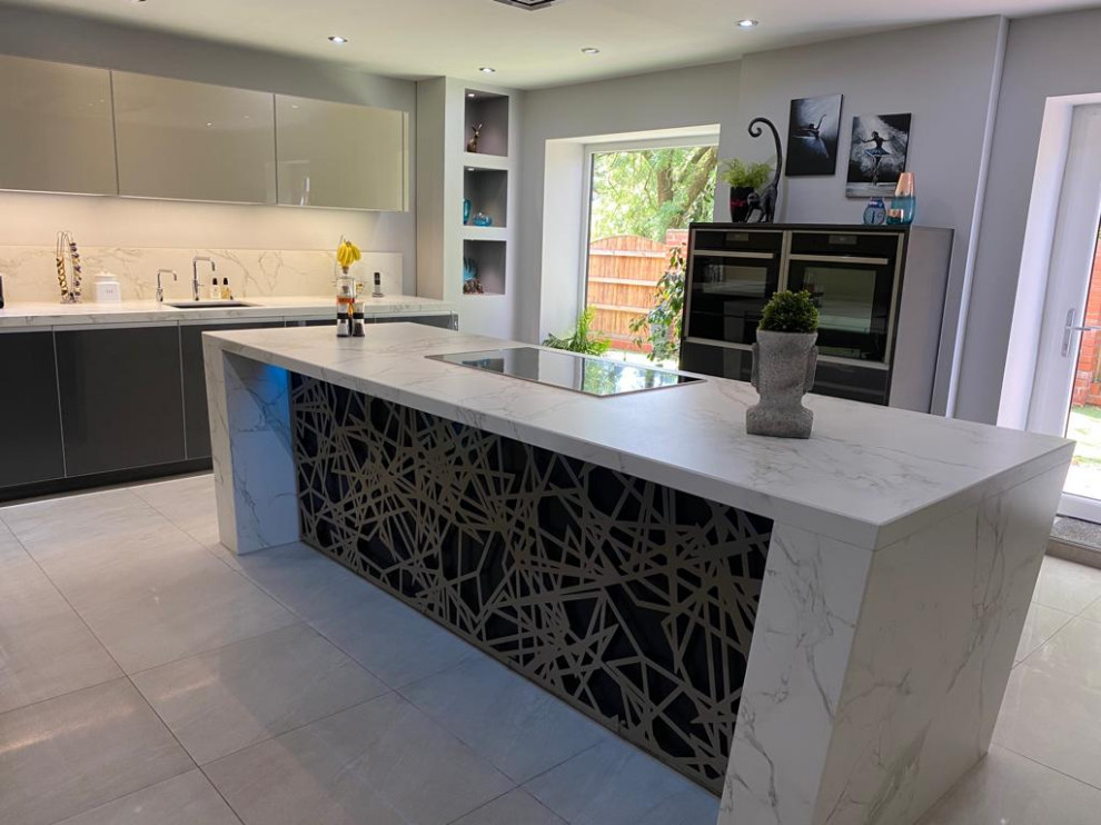 Medium sized contemporary grey and white galley kitchen in Manchester with a submerged sink, glass-front cabinets, grey cabinets, quartz worktops, stone slab splashback, stainless steel appliances, porcelain flooring, an island, beige floors and white worktops.