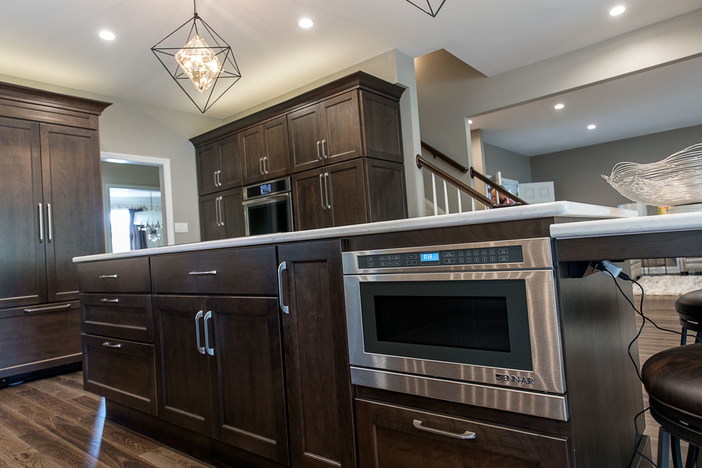 Inspiration for a large transitional l-shaped medium tone wood floor and brown floor eat-in kitchen remodel with an undermount sink, flat-panel cabinets, dark wood cabinets, marble countertops, white backsplash, ceramic backsplash, stainless steel appliances, an island and white countertops