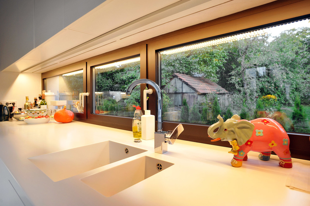 Große Moderne Wohnküche in L-Form mit weißen Schränken, Küchenrückwand in Weiß, integriertem Waschbecken, flächenbündigen Schrankfronten, Mineralwerkstoff-Arbeitsplatte, Rückwand aus Zementfliesen, Küchengeräten aus Edelstahl, Betonboden, Halbinsel und grauem Boden in Berlin