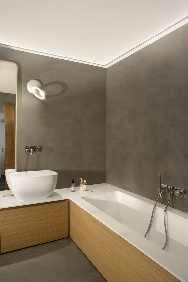 Inspiration for a contemporary ensuite bathroom in Turin with flat-panel cabinets, light wood cabinets, a submerged bath, grey tiles, grey walls, concrete flooring, a vessel sink, solid surface worktops and grey floors.