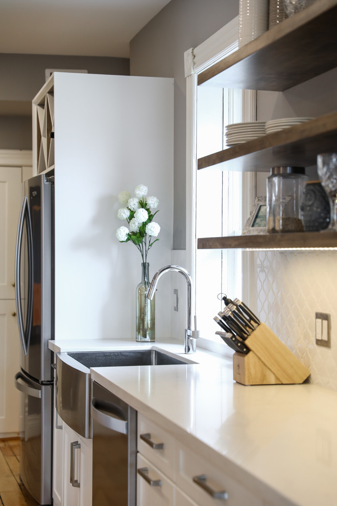 Mid-sized transitional single-wall medium tone wood floor and brown floor eat-in kitchen photo with a farmhouse sink, shaker cabinets, white cabinets, white backsplash, stainless steel appliances, an island and white countertops