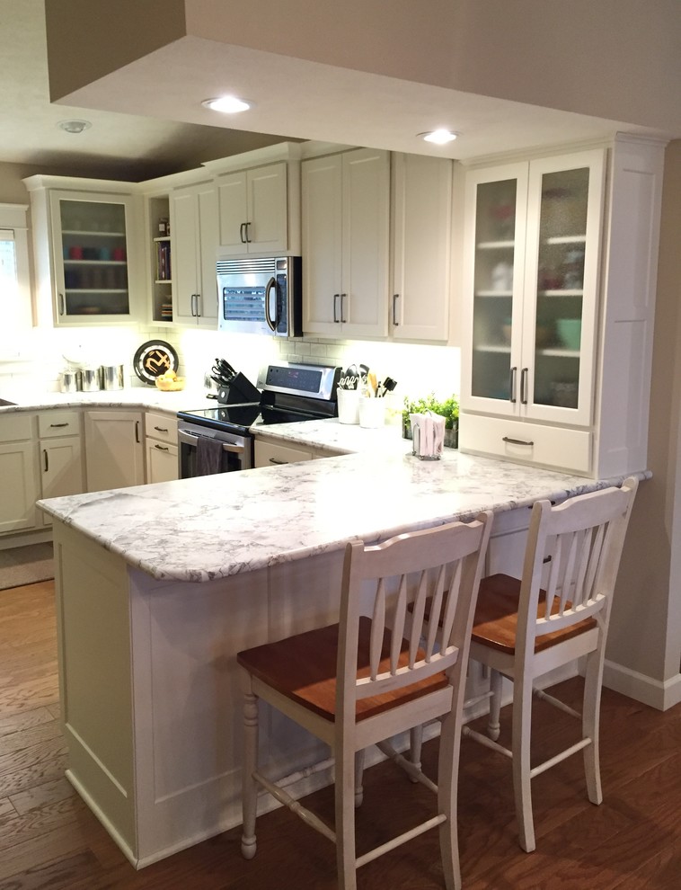 Example of a mid-sized transitional u-shaped medium tone wood floor eat-in kitchen design with an integrated sink, shaker cabinets, white cabinets, laminate countertops, white backsplash, subway tile backsplash, stainless steel appliances and a peninsula