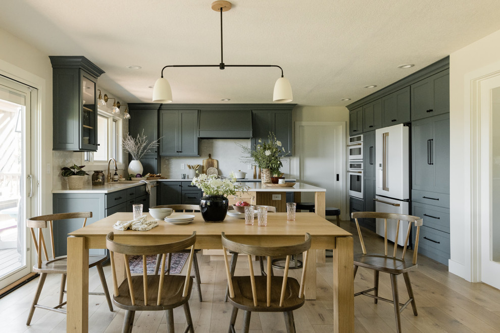 Klassische Küche in U-Form mit Unterbauwaschbecken, Küchenrückwand in Weiß, weißen Elektrogeräten, hellem Holzboden, Kücheninsel und weißer Arbeitsplatte in Sonstige