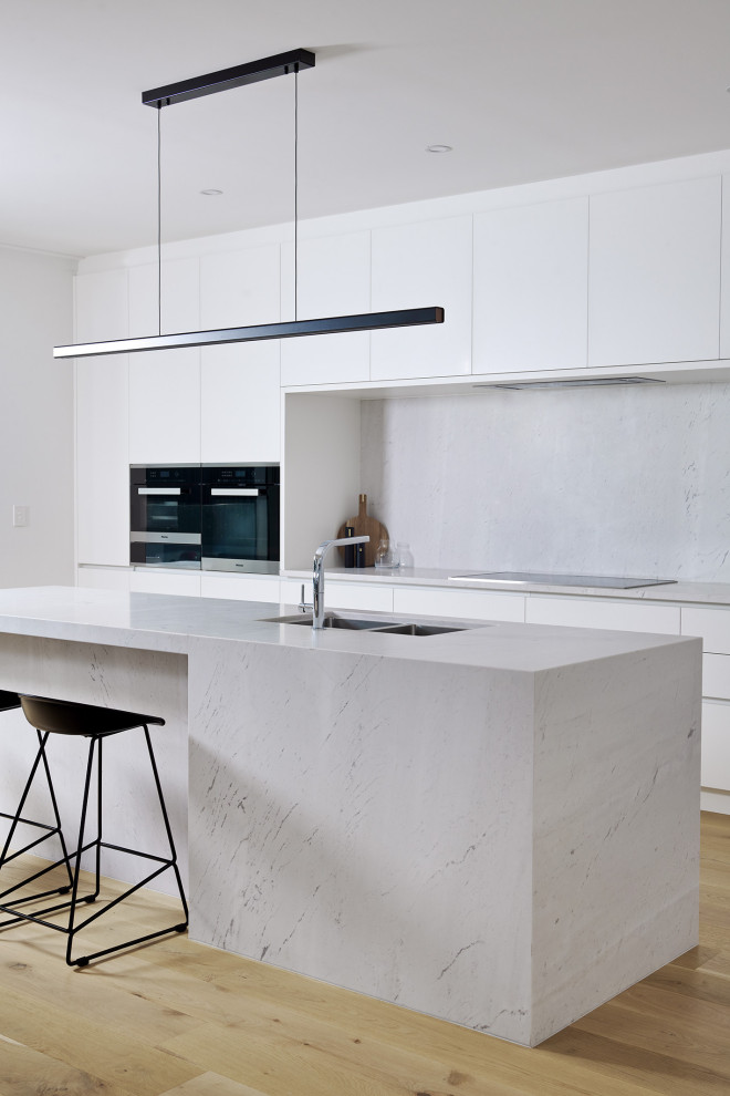 Inspiration for a large modern galley eat-in kitchen in Perth with a double-bowl sink, flat-panel cabinets, white cabinets, marble benchtops, white splashback, marble splashback, black appliances, light hardwood floors, with island, yellow floor and white benchtop.