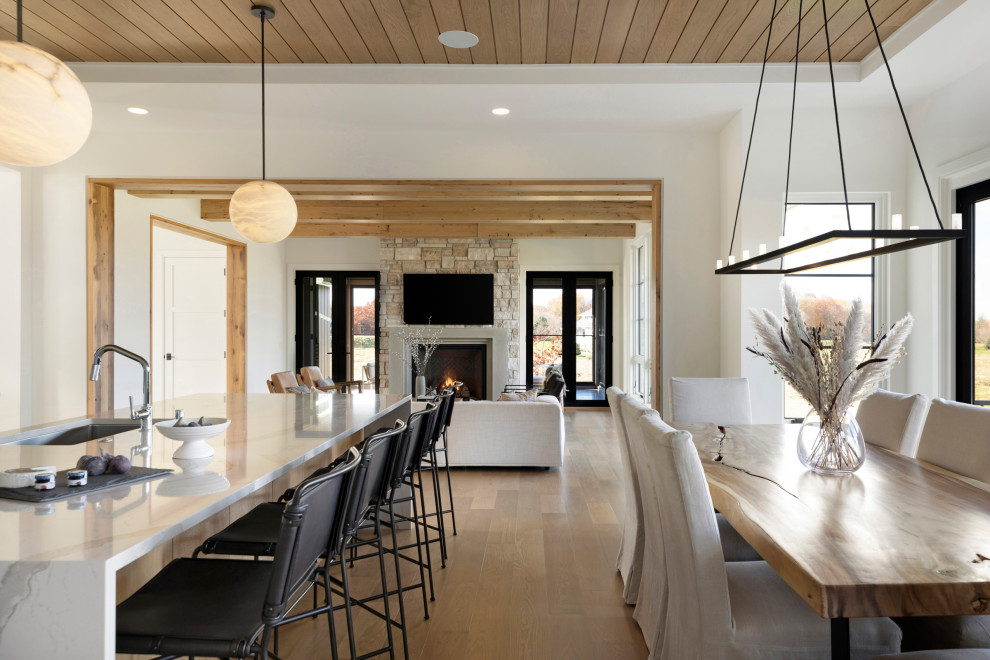Design ideas for a country kitchen/dining combo in Minneapolis with white walls, light hardwood floors, a standard fireplace, a stone fireplace surround, brown floor and timber.