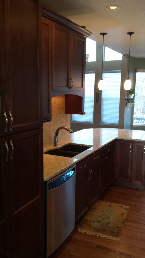 Kitchen - medium tone wood floor kitchen idea in Denver with a double-bowl sink, recessed-panel cabinets, dark wood cabinets and stainless steel appliances