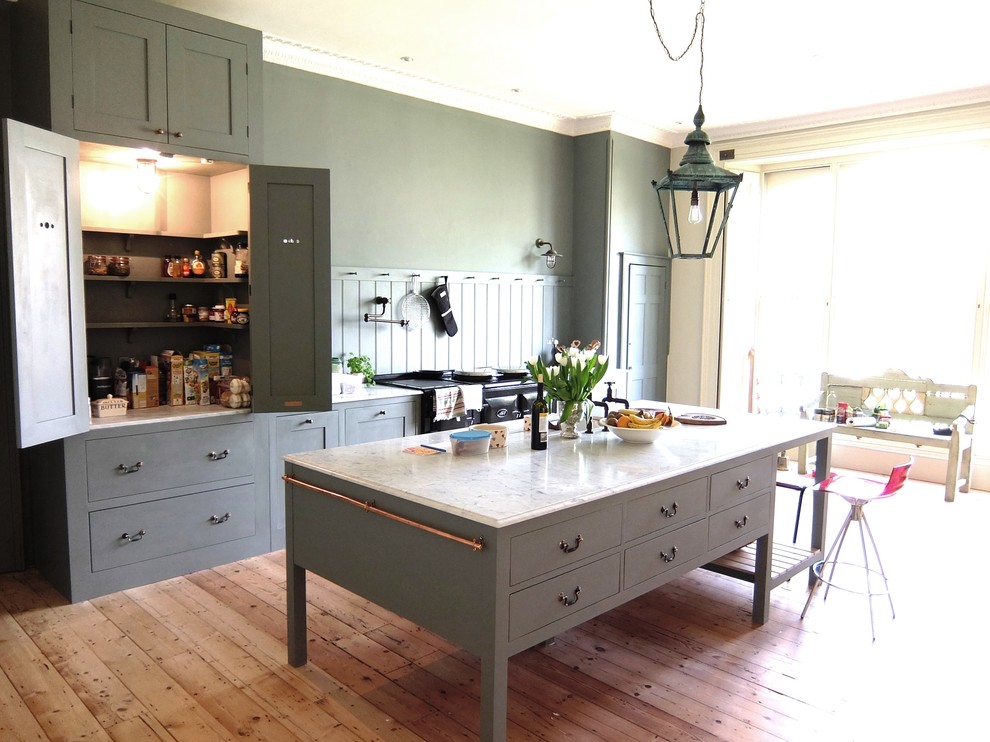 Expansive arts and crafts open plan kitchen in London with a farmhouse sink, shaker cabinets, grey cabinets, marble benchtops, grey splashback, with island and black appliances.
