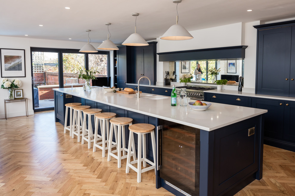 Photo of a transitional galley kitchen in Berkshire with a double-bowl sink, shaker cabinets, blue cabinets, white splashback, medium hardwood floors, with island and brown floor.
