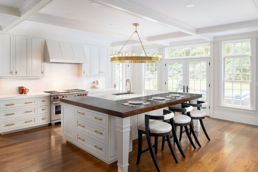 Design ideas for a transitional l-shaped open plan kitchen in Providence with an undermount sink, shaker cabinets, white cabinets, wood benchtops, white splashback, stainless steel appliances, medium hardwood floors, with island, brown floor and white benchtop.