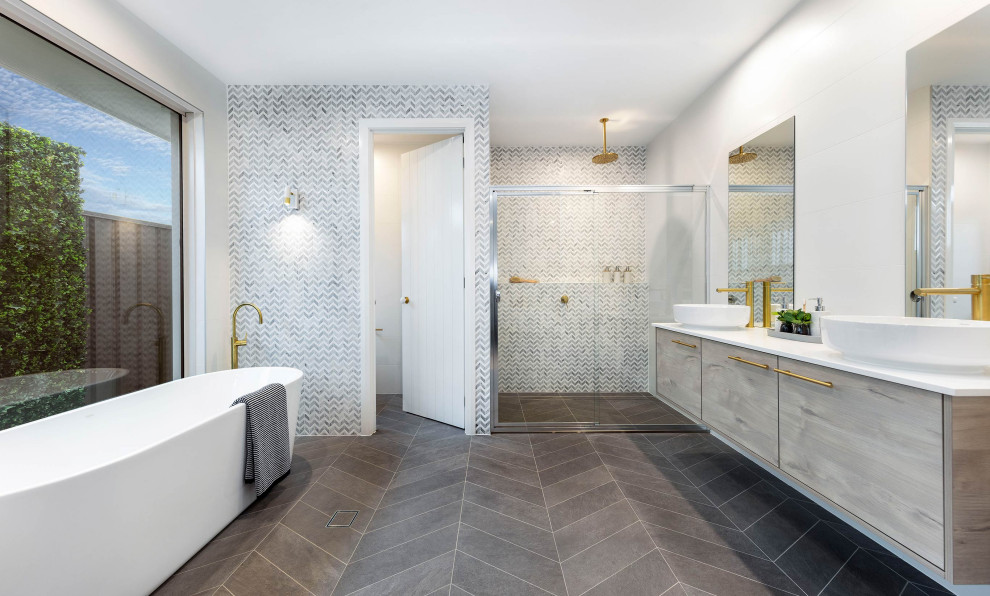 Photo of a mid-sized contemporary master bathroom in Other with shaker cabinets, white cabinets, a freestanding tub, a corner shower, gray tile, ceramic tile, white walls, ceramic floors, a drop-in sink, engineered quartz benchtops, grey floor, a hinged shower door and white benchtops.