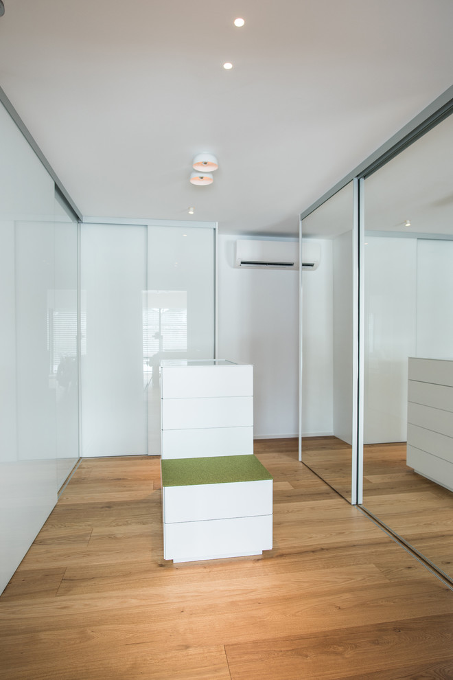 Photo of a mid-sized modern gender-neutral walk-in wardrobe in Stuttgart with flat-panel cabinets, white cabinets, medium hardwood floors and brown floor.