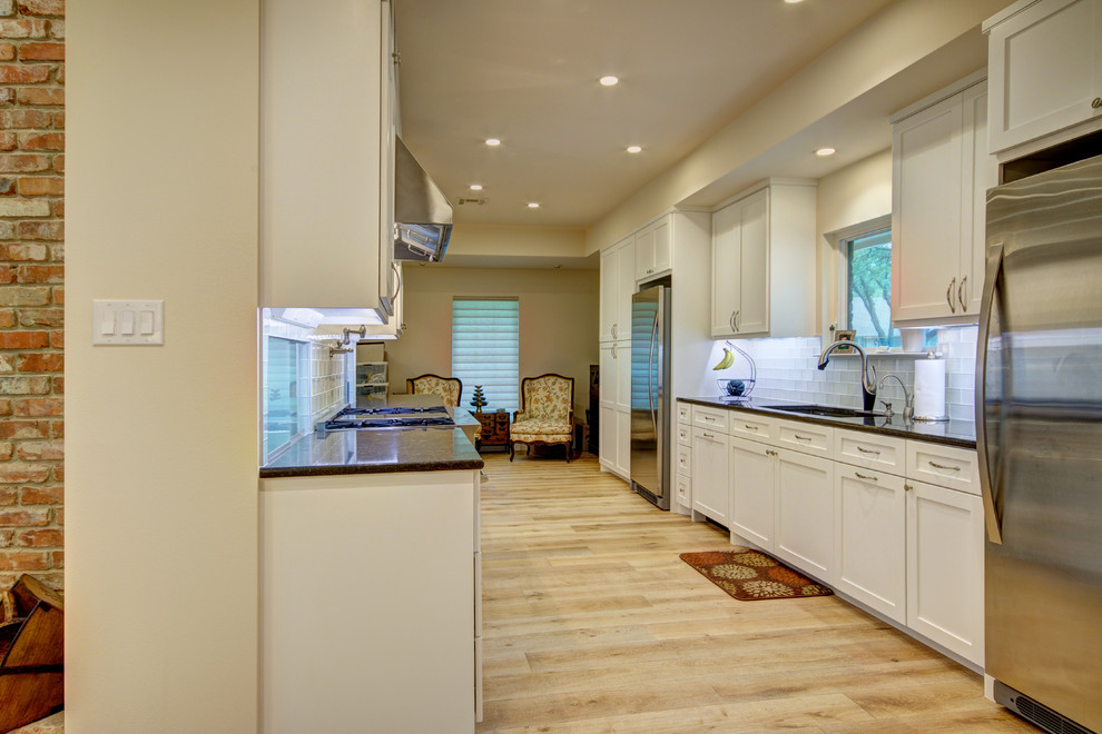 Inspiration for a mid-sized transitional galley light wood floor eat-in kitchen remodel in Austin with an undermount sink, shaker cabinets, white cabinets, granite countertops, white backsplash, glass tile backsplash, stainless steel appliances and no island