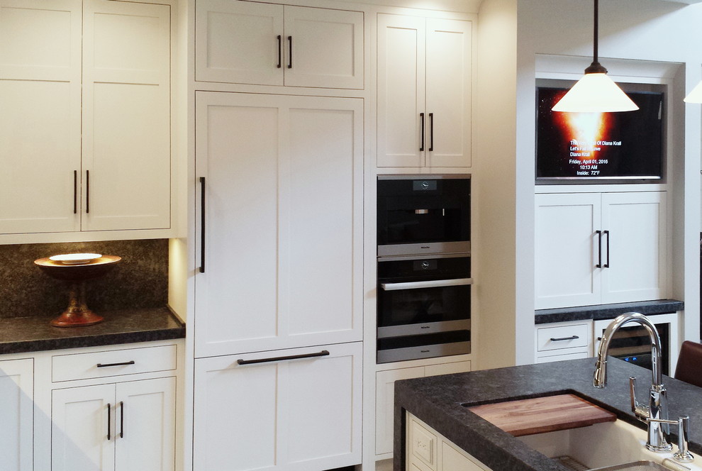 Inspiration for a mid-sized transitional l-shaped concrete floor and beige floor eat-in kitchen remodel with an undermount sink, shaker cabinets, white cabinets, granite countertops, black backsplash, stone slab backsplash, paneled appliances and a peninsula