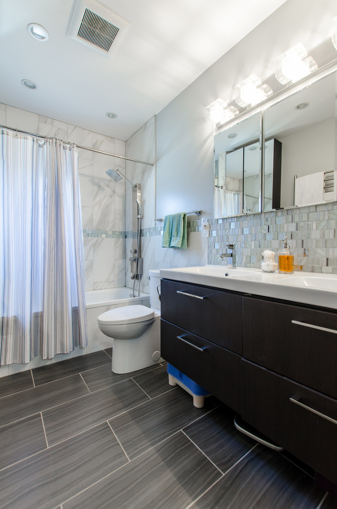 Photo of a mid-sized transitional master bathroom in New York with flat-panel cabinets, black cabinets, an alcove tub, a shower/bathtub combo, a one-piece toilet, blue tile, gray tile, white tile, mosaic tile, blue walls, laminate floors, an integrated sink, grey floor and a shower curtain.
