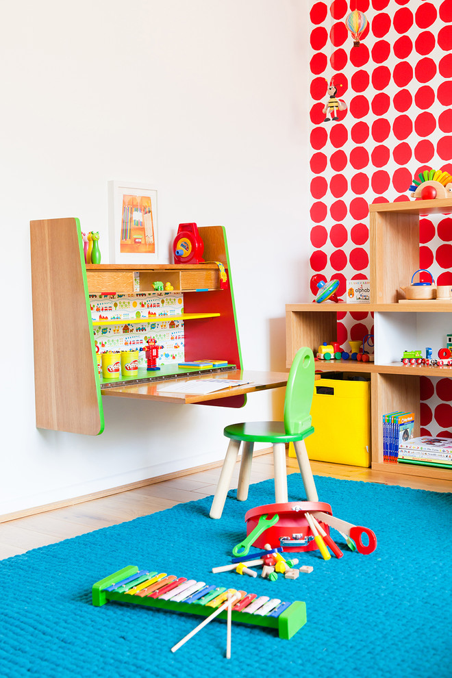 This is an example of a mid-sized contemporary gender-neutral kids' bedroom for kids 4-10 years old in Cambridgeshire with light hardwood floors and red walls.