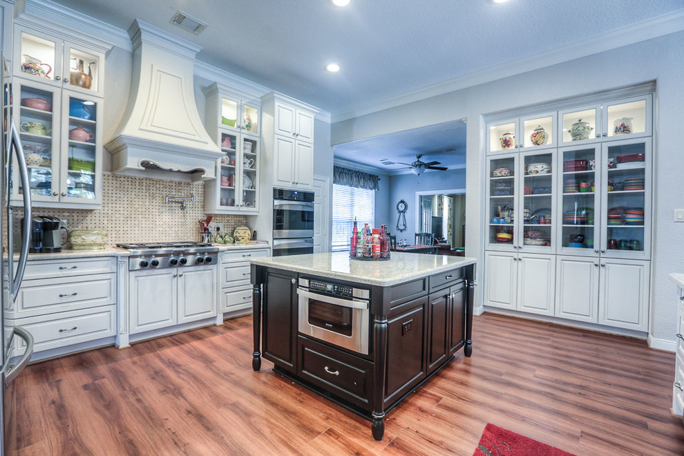 Photo of a mid-sized traditional galley separate kitchen in Houston with an undermount sink, raised-panel cabinets, white cabinets, granite benchtops, multi-coloured splashback, ceramic splashback, stainless steel appliances, medium hardwood floors and with island.