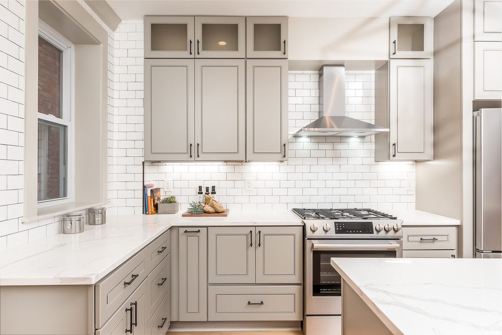 Photo of a transitional l-shaped kitchen in DC Metro with grey cabinets, white splashback, stainless steel appliances, with island, white benchtop and recessed-panel cabinets.
