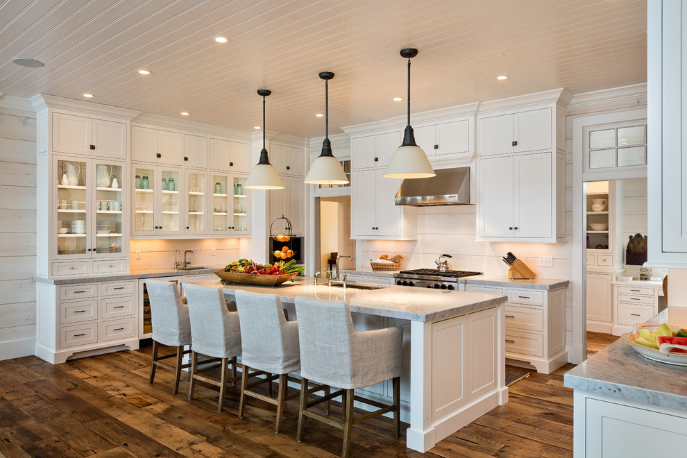 Design ideas for a large traditional u-shaped kitchen in Milwaukee with an undermount sink, glass-front cabinets, white cabinets, white splashback, medium hardwood floors, with island, timber splashback, stainless steel appliances and brown floor.