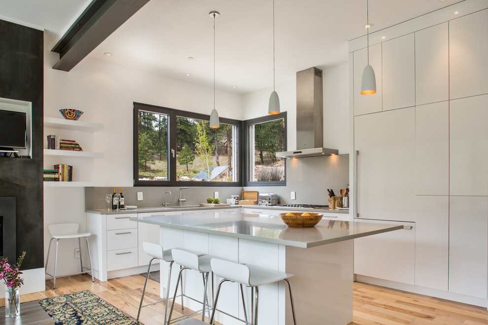 This is an example of a contemporary l-shaped open plan kitchen in Denver with an undermount sink, flat-panel cabinets, white cabinets, grey splashback, panelled appliances, light hardwood floors, with island and beige floor.