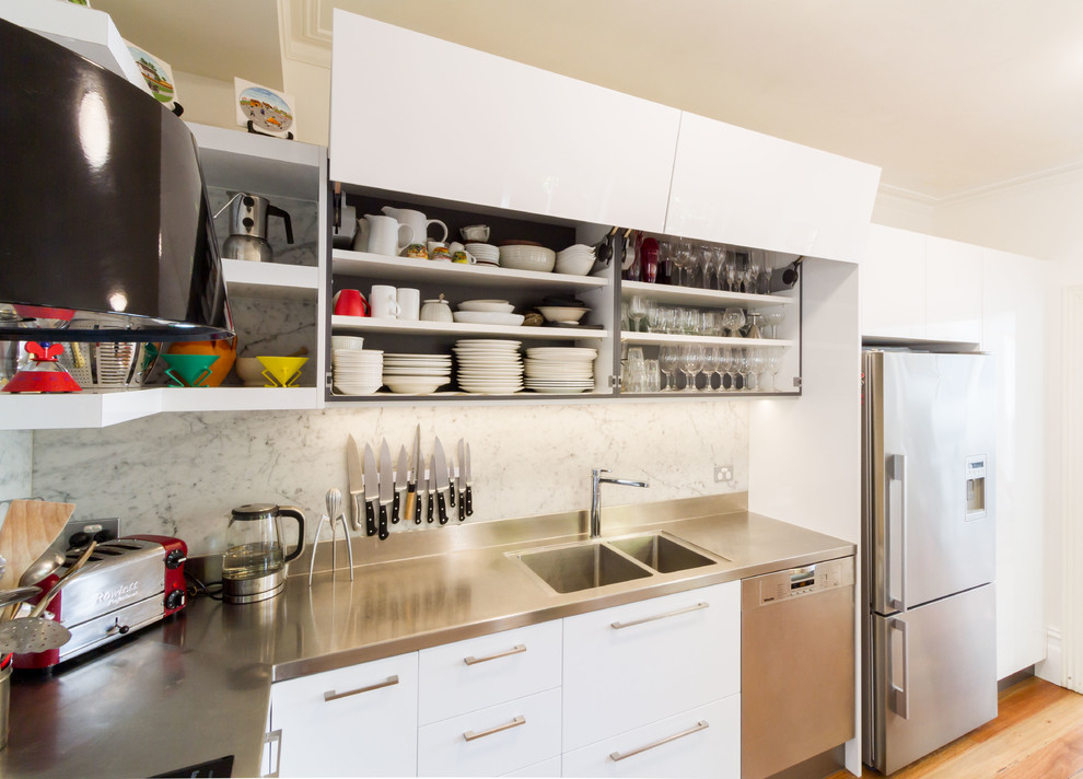 Inspiration for a small contemporary l-shaped kitchen pantry in Melbourne with an integrated sink, flat-panel cabinets, white cabinets, stainless steel benchtops, white splashback, marble splashback, stainless steel appliances, medium hardwood floors and brown floor.