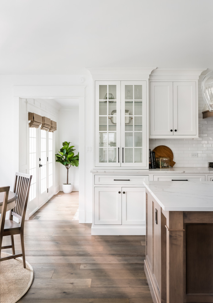 Design ideas for a large country eat-in kitchen in Chicago with a farmhouse sink, shaker cabinets, white cabinets, quartz benchtops, white splashback, window splashback, stainless steel appliances, medium hardwood floors, with island, brown floor and white benchtop.