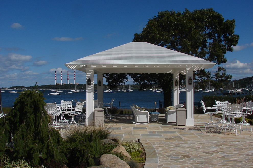 Beach style backyard patio in New York with natural stone pavers and a pergola.