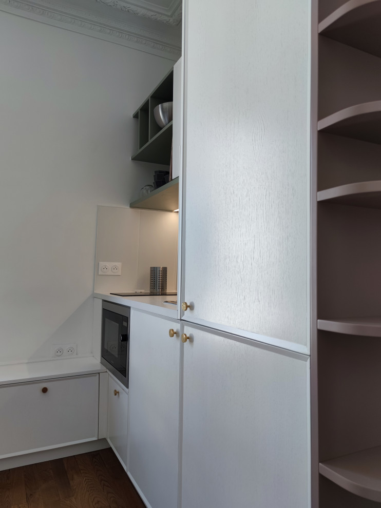 Inspiration för små moderna linjära vitt kök med öppen planlösning, med en enkel diskho, luckor med profilerade fronter, vita skåp, bänkskiva i kvartsit, vitt stänkskydd, rostfria vitvaror, ljust trägolv och brunt golv