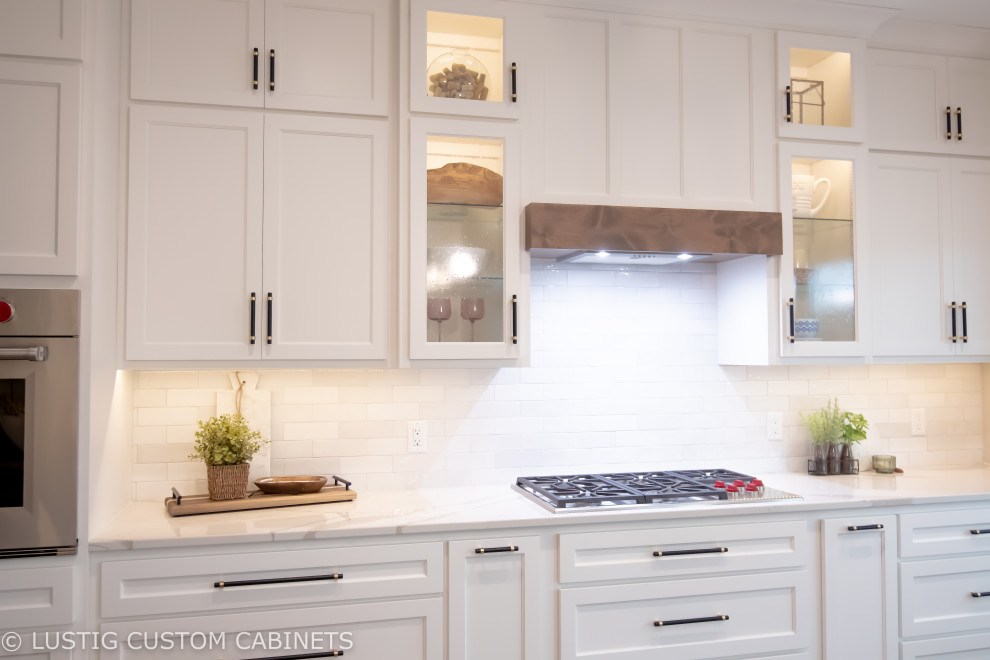 Example of a large transitional l-shaped laminate floor and brown floor open concept kitchen design with an undermount sink, flat-panel cabinets, white cabinets, quartz countertops, white backsplash, ceramic backsplash, stainless steel appliances, an island and white countertops