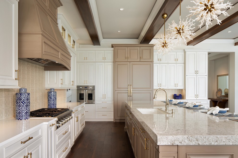 This is an example of a large beach style l-shaped open plan kitchen in Miami with an undermount sink, raised-panel cabinets, white cabinets, beige splashback, panelled appliances, dark hardwood floors, with island, brown floor and beige benchtop.