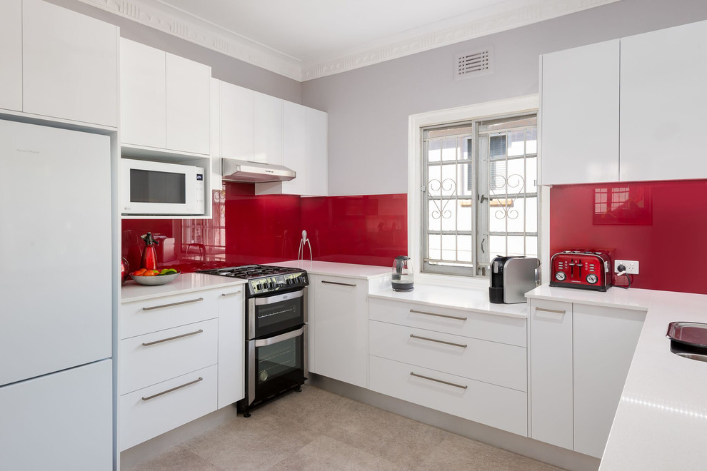 Inspiration for a mid-sized modern u-shaped eat-in kitchen in Auckland with an undermount sink, white cabinets, solid surface benchtops, red splashback, glass sheet splashback, coloured appliances, porcelain floors, beige floor and white benchtop.