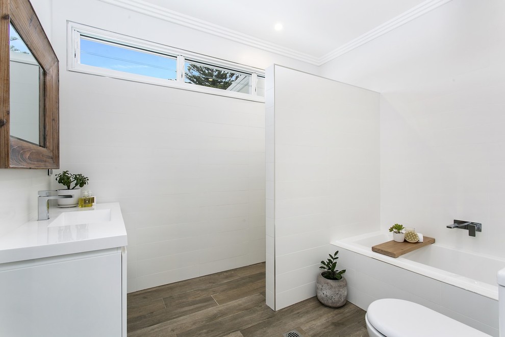 Inspiration for a beach style bathroom in Sydney with flat-panel cabinets, white cabinets, an alcove tub, an open shower, a two-piece toilet, white tile, white walls and an integrated sink.
