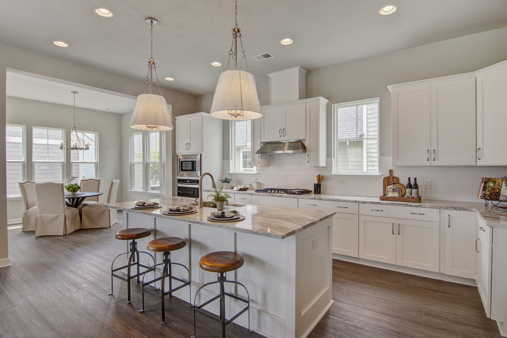 Photo of a transitional l-shaped eat-in kitchen in Charleston with an undermount sink, shaker cabinets, white cabinets, white splashback, subway tile splashback, stainless steel appliances, medium hardwood floors, with island, brown floor and grey benchtop.