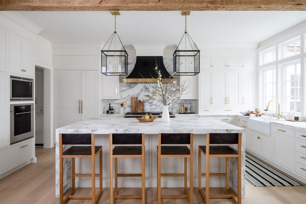 Transitional u-shaped open plan kitchen in New York with a farmhouse sink, shaker cabinets, white cabinets, marble benchtops, multi-coloured splashback, marble splashback, panelled appliances, light hardwood floors, with island, multi-coloured benchtop and white floor.