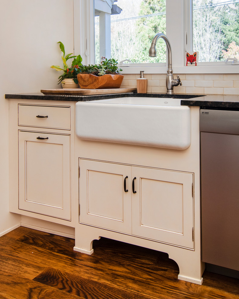 Transitional u-shaped medium tone wood floor kitchen photo in New York with a farmhouse sink, beaded inset cabinets, white cabinets, granite countertops, beige backsplash, subway tile backsplash, stainless steel appliances and an island
