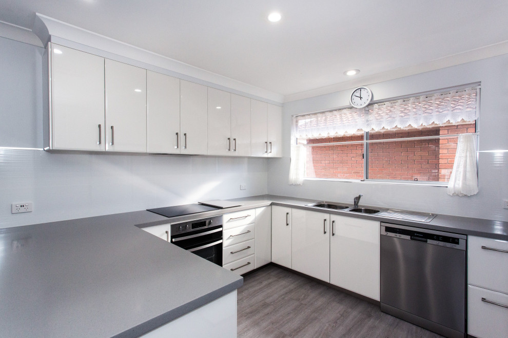 Mid-sized contemporary u-shaped eat-in kitchen in Other with a double-bowl sink, flat-panel cabinets, white cabinets, solid surface benchtops, white splashback, ceramic splashback, white appliances, laminate floors, a peninsula, grey floor and grey benchtop.