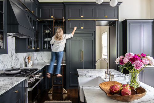 Homeowner assembling and installing dark shaker RTA cabinets with marble countertops in a modern Canadian kitchen