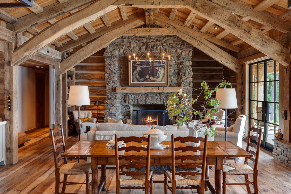 Esempio di una sala da pranzo aperta verso il soggiorno rustica con cornice del camino in pietra, travi a vista e pareti in legno