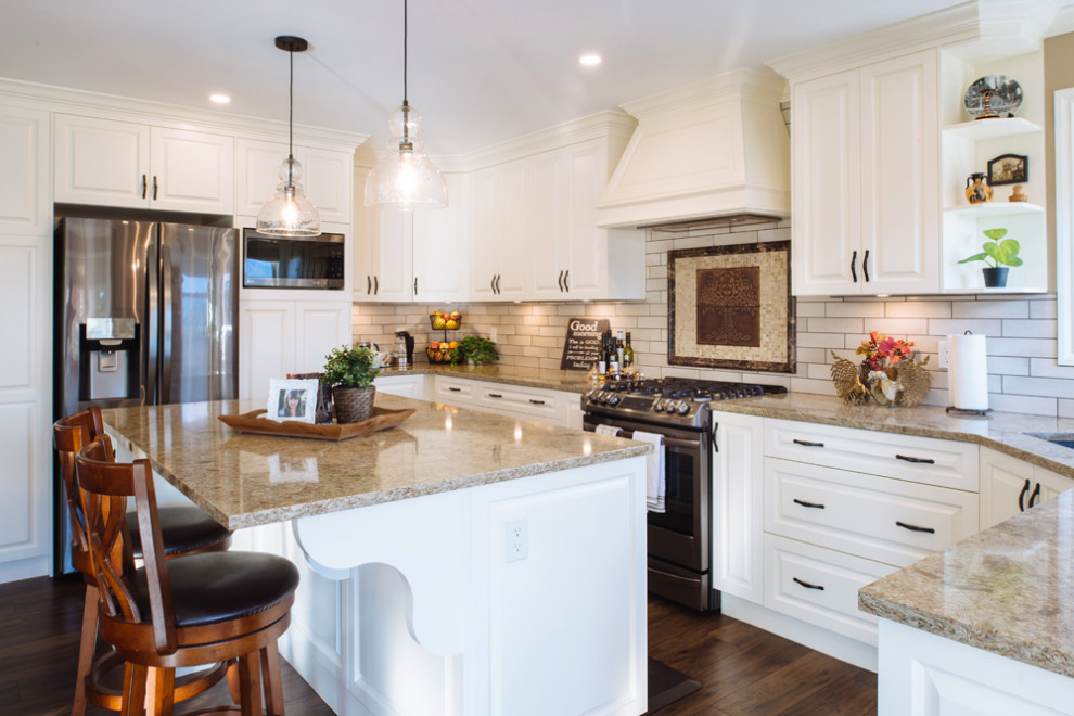 This is an example of a large u-shaped eat-in kitchen in Vancouver with an undermount sink, raised-panel cabinets, white cabinets, quartz benchtops, white splashback, subway tile splashback, stainless steel appliances, vinyl floors, with island, brown floor and beige benchtop.