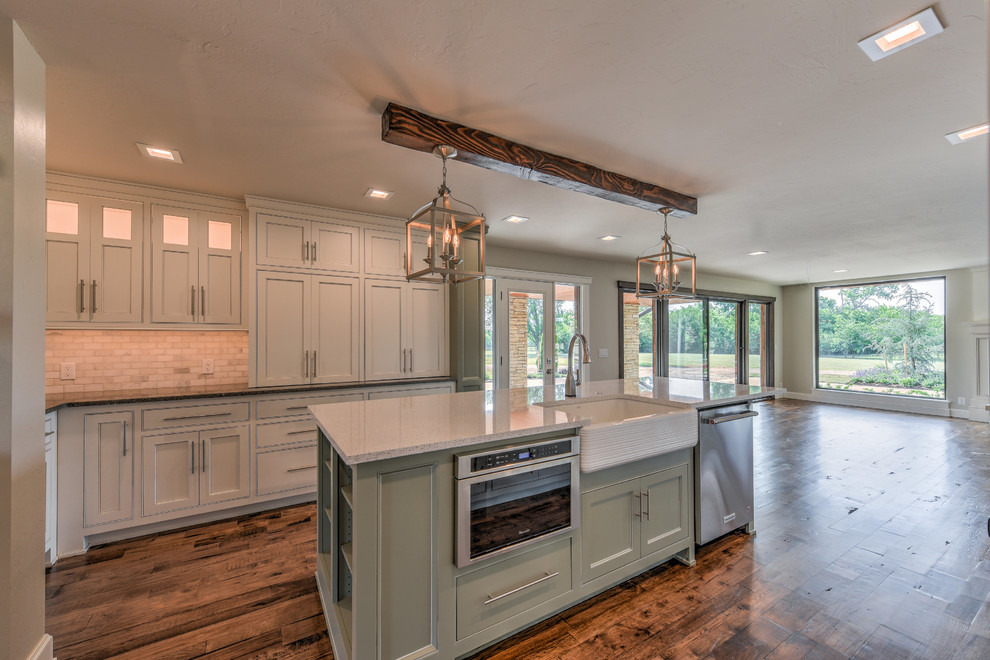 Photo of a large country u-shaped open plan kitchen in Oklahoma City with an undermount sink, shaker cabinets, white cabinets, quartz benchtops, white splashback, subway tile splashback, stainless steel appliances, dark hardwood floors, with island and brown floor.