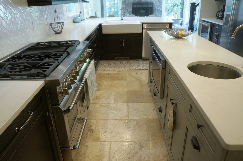 Eat-in kitchen - mid-sized transitional l-shaped travertine floor eat-in kitchen idea in Raleigh with a farmhouse sink, flat-panel cabinets, dark wood cabinets, quartz countertops, white backsplash, ceramic backsplash, stainless steel appliances and an island