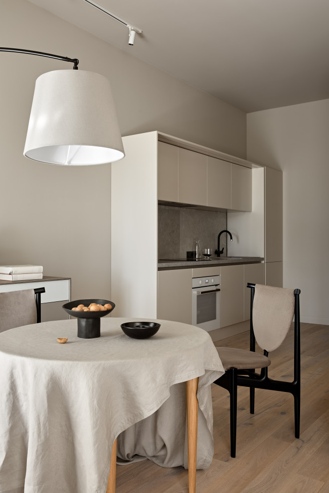 Photo of a small contemporary single-wall eat-in kitchen in Saint Petersburg with a single-bowl sink, flat-panel cabinets, beige cabinets, wood benchtops, grey splashback, porcelain splashback, white appliances, medium hardwood floors, brown floor and grey benchtop.