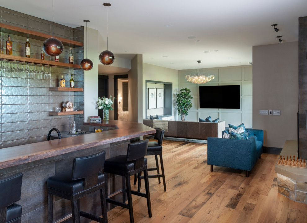 This is an example of a large arts and crafts open concept family room in Denver with a home bar, multi-coloured walls, light hardwood floors, a two-sided fireplace, a tile fireplace surround, a wall-mounted tv and multi-coloured floor.