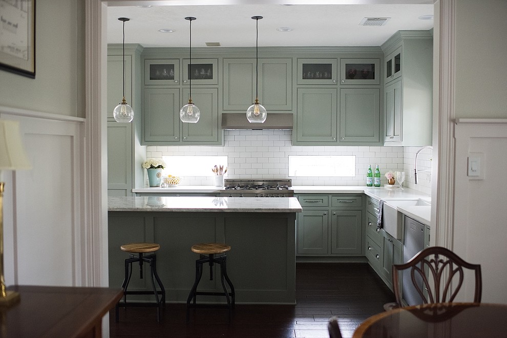 Mid-sized country l-shaped eat-in kitchen in Houston with a farmhouse sink, recessed-panel cabinets, green cabinets, quartzite benchtops, white splashback, subway tile splashback, stainless steel appliances, dark hardwood floors, with island and brown floor.