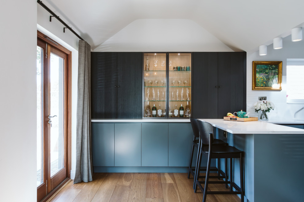 Inspiration for a mid-sized contemporary l-shaped seated home bar in Surrey with flat-panel cabinets, blue cabinets, solid surface benchtops, medium hardwood floors, beige floor and white benchtop.