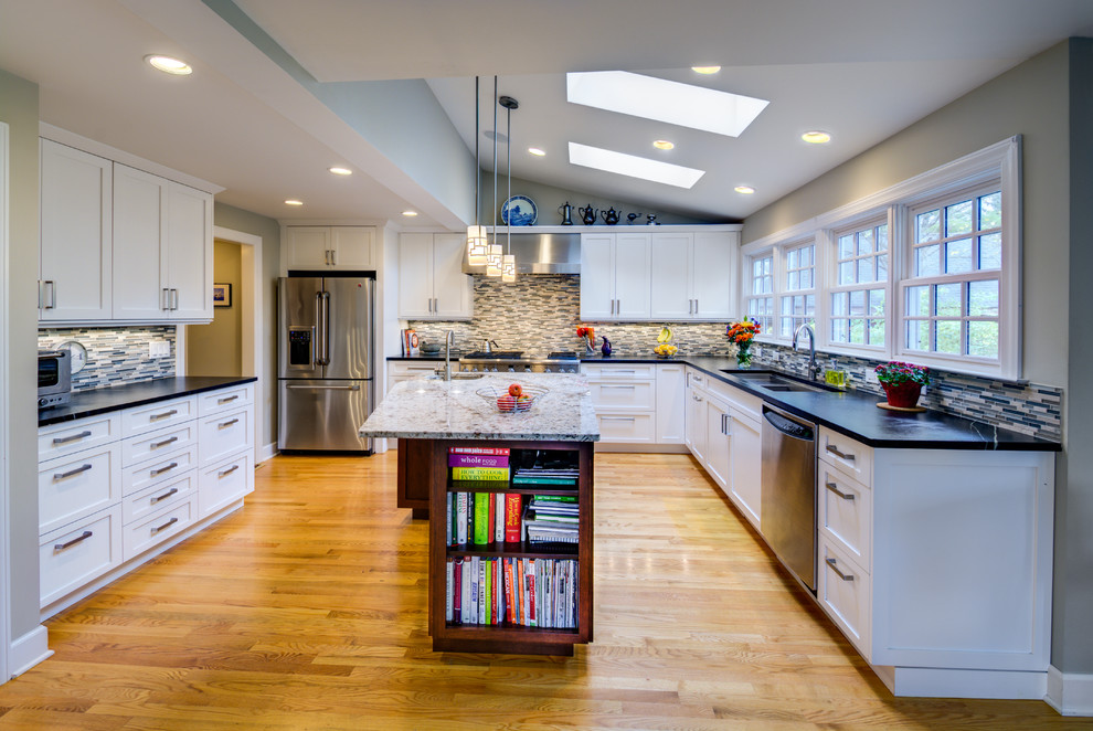 This is an example of a mid-sized traditional l-shaped open plan kitchen in Detroit with an undermount sink, recessed-panel cabinets, white cabinets, soapstone benchtops, grey splashback, ceramic splashback, stainless steel appliances, medium hardwood floors and with island.