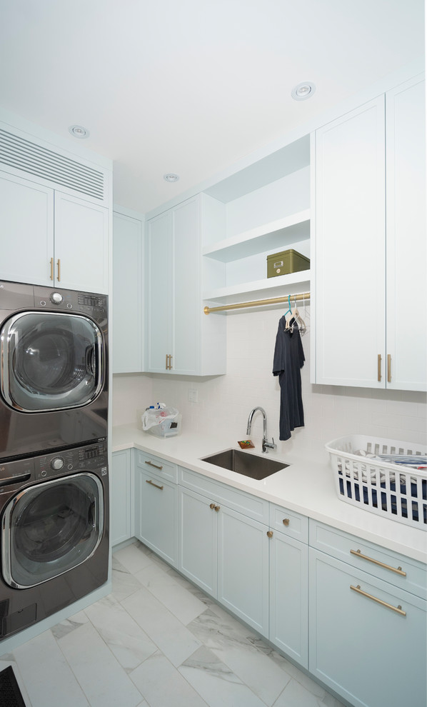 This is an example of a mid-sized contemporary l-shaped dedicated laundry room with an undermount sink, shaker cabinets, white cabinets, white walls, a stacked washer and dryer, white floor and white benchtop.