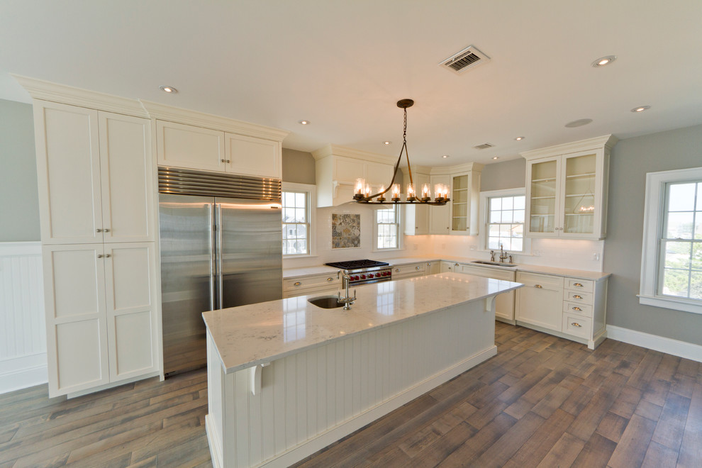 This is an example of a beach style kitchen in New York with a drop-in sink, white splashback, subway tile splashback, stainless steel appliances, light hardwood floors and white floor.