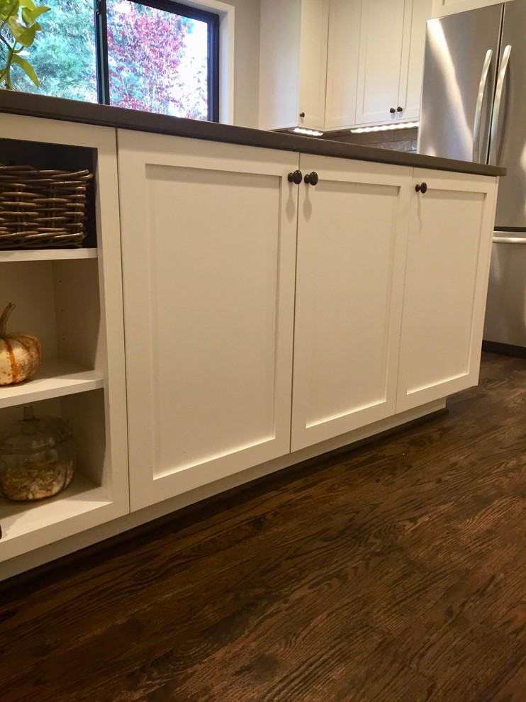 Inspiration for a mid-sized traditional l-shaped open plan kitchen in Portland with an undermount sink, shaker cabinets, white cabinets, quartz benchtops, beige splashback, subway tile splashback, stainless steel appliances, medium hardwood floors, with island and brown benchtop.